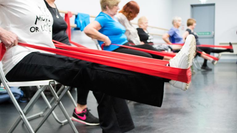 Women seated in exercise class using stretch bands on their legs.